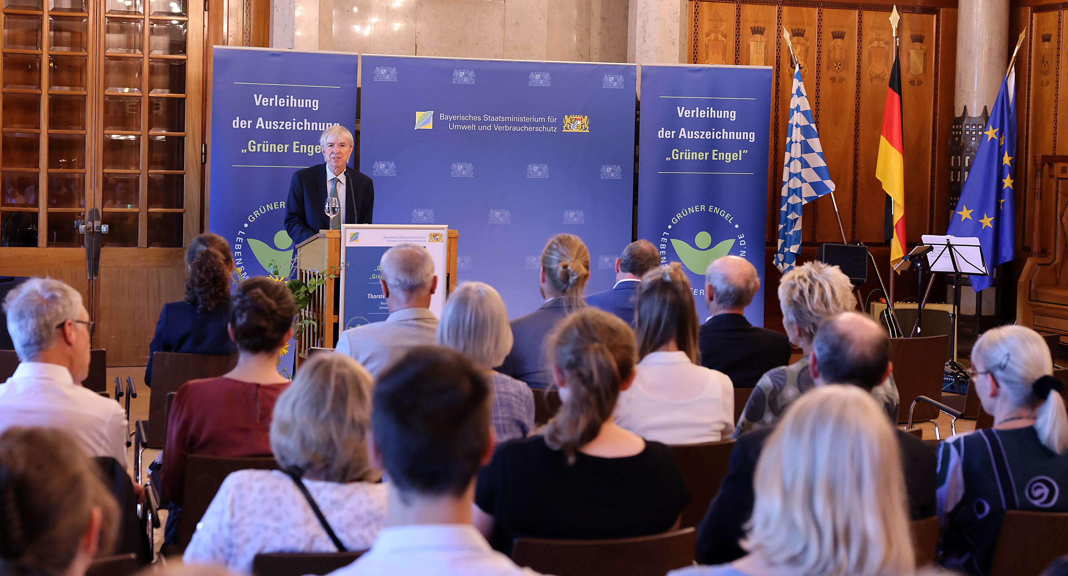Thomas Engel, Regierungsvizepräsident der Regierung von Oberfranken, steht vor einer dunkelblauen Wand an einem Rednerpult. Davor sitzen mit dem Rücken zum Fotografen mehrere Zuhörerinnen und Zuhörer.