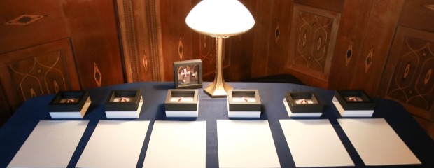 Sechs Orden und sechs Urkunden liegen nebeneinander aufgereiht auf einer blauen Tischdecke.