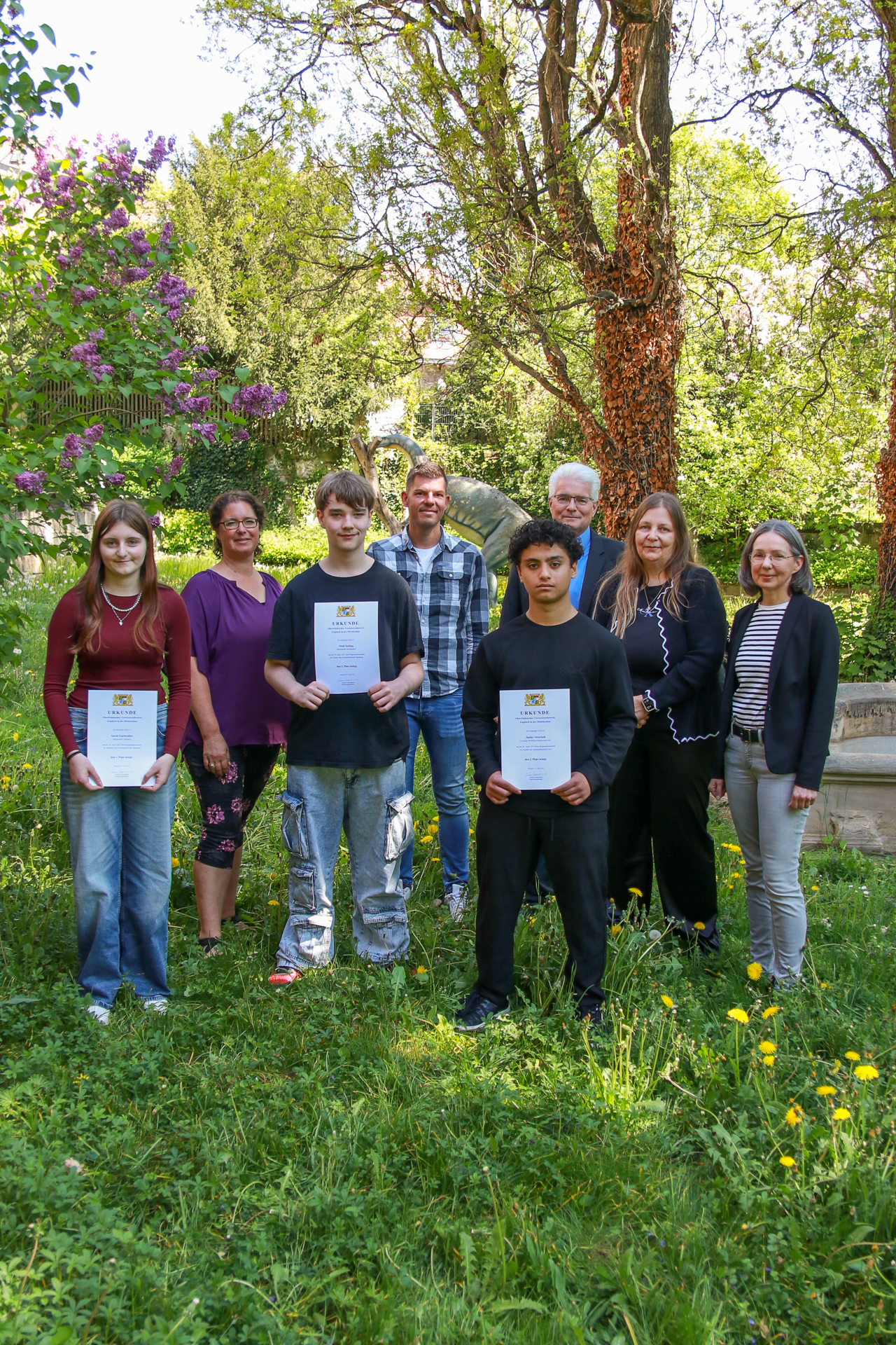 Die Siegerin und die zwei Sieger des oberfränkischen Vorlesewettbe-werbs in Englisch, v.l.: Sarah Fairbrother (1. Platz), Christine Norwood (Jury), Noah Seuling (3. Platz), Stefan Klerner (Jury), Jaafar Alzarkali (2. Platz), Stefan Kuen (Abteilungsdirektor Schulen - Regierung von Oberfranken), Simone Weiner (Jury), Kathrin Sigg (SG 40.1 - Regierung von Oberfranken) Frühlingswiese mit Foto der drei Bestplatzierten