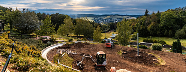 Baustelle mit Baggern in einem großen Erdloch mitten in grüner Natur
