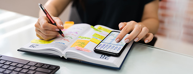 Termine und Veranstaltungen Eine Frau streicht in ihrem Kalender Termine an und vergleicht diese mit ihrem Handy