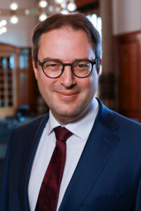 Portraitfoto des Regierungspräsidenten Florian Luderschmid Regierungspräsident Florian Luderschmid in blauem Sakko, weißem Hemd und dunkelroter Krawatte, abgelichtet im Landratssaal der Regierung von Oberfranken